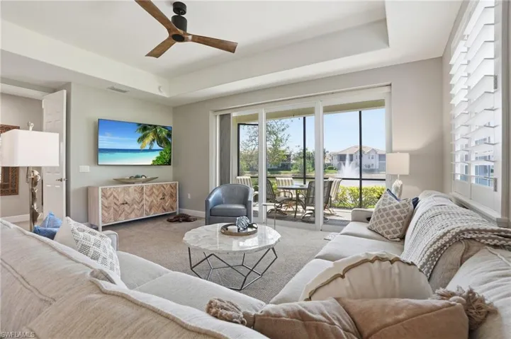 Living area featuring a raised ceiling, carpet flooring, and a ceiling fan