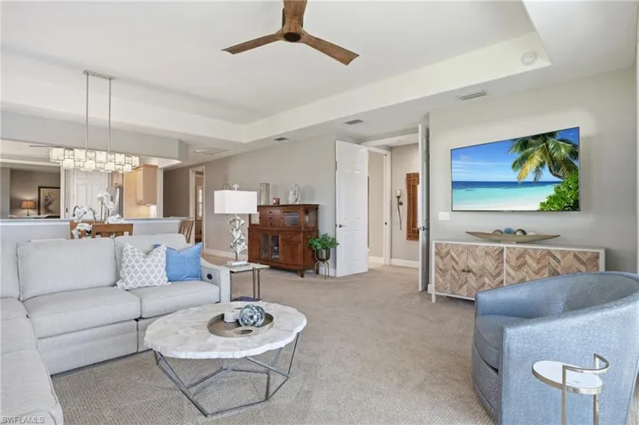 Living area with a ceiling fan, a tray ceiling, and light carpet