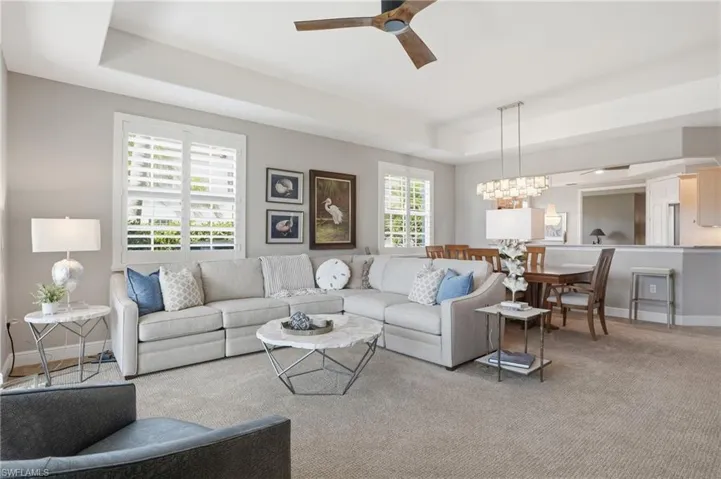 Carpeted living room featuring a tray ceiling, ceiling fan, and suspended lighting