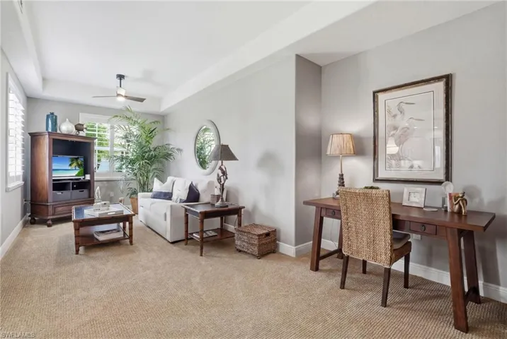 Living room with a raised ceiling, light colored carpet, and a ceiling fan