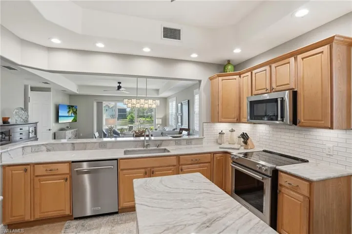 Kitchen featuring a tray ceiling, stainless steel appliances, light stone counters, a ceiling fan, and open floor plan