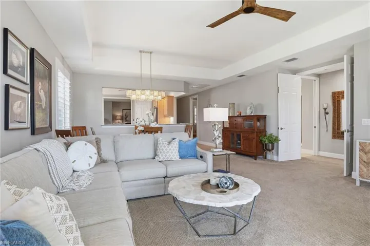 Living room featuring ceiling fan, a tray ceiling, light colored carpet, and hanging lights