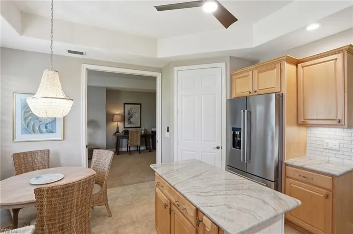 Kitchen with high quality fridge, a ceiling fan, light wood finish cabinets, light stone countertops, and tasteful backsplash