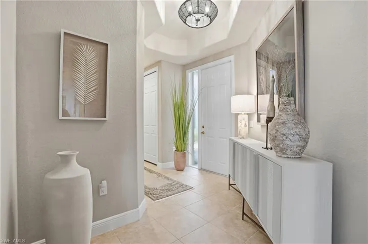 Foyer entrance with a textured wall, a tray ceiling, and light tile patterned flooring