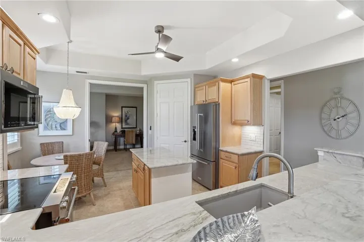 Kitchen featuring a raised ceiling, stainless steel appliances, light wood finish cabinets, tasteful backsplash, and light stone countertops