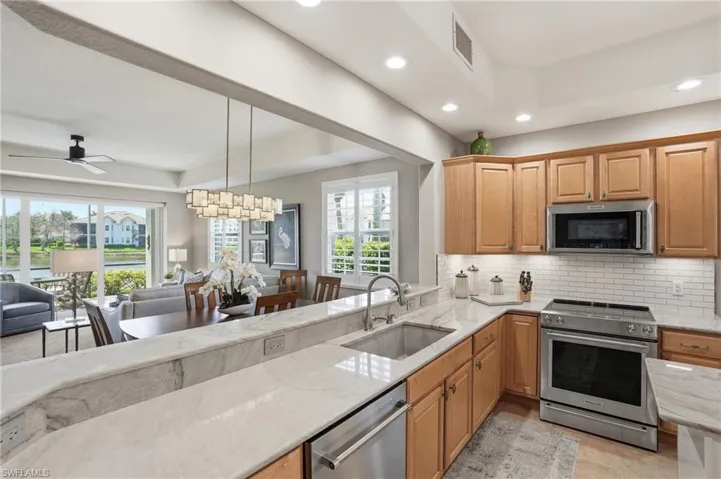 Kitchen featuring stainless steel appliances, open floor plan, light stone counters, a ceiling fan, and a raised ceiling