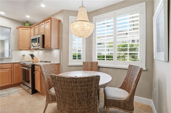 Kitchen featuring stainless steel appliances, tasteful backsplash, hanging lights, light stone counters, and light tile patterned flooring