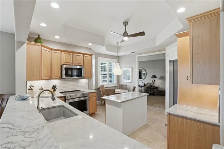 Kitchen with a raised ceiling, stainless steel appliances, light wood finish cabinetry, a center island, and a ceiling fan