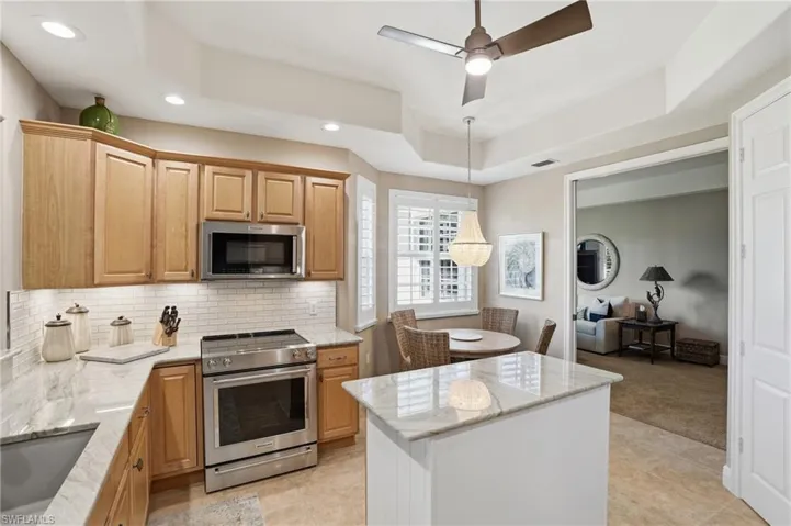 Kitchen featuring a tray ceiling, stainless steel appliances, light stone countertops, a ceiling fan, and decorative light fixtures