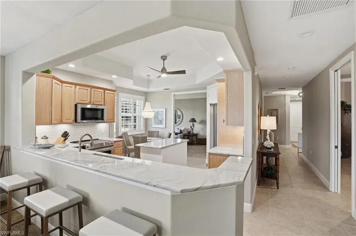 Kitchen with a kitchen island, light wood finish cabinetry, backsplash, a ceiling fan, and light stone counters