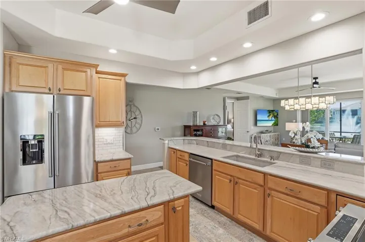 Kitchen featuring ceiling fan, stainless steel appliances, a raised ceiling, open floor plan, and light wood finish cabinetry