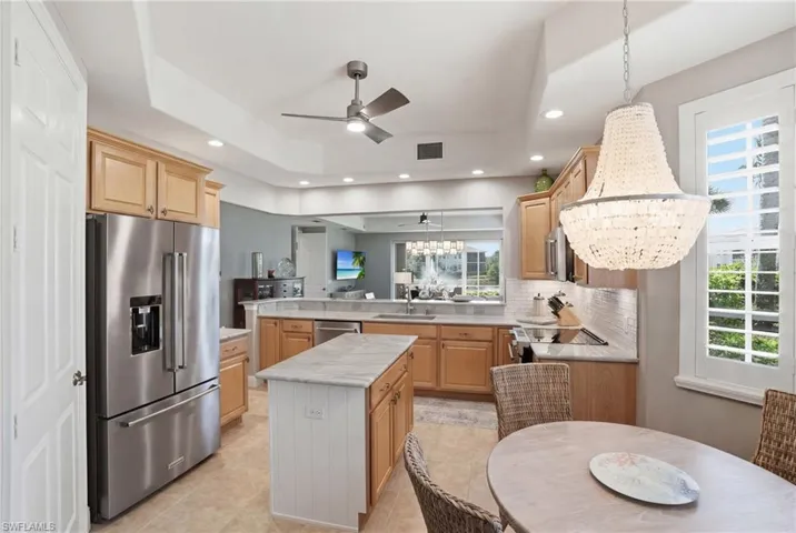 Kitchen featuring a peninsula, stainless steel appliances, a ceiling fan, a center island, and light wood finish cabinetry