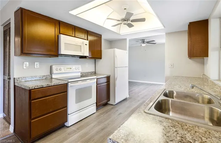 Kitchen featuring light wood-type flooring, white appliances, a tray ceiling, sink, and ceiling fan