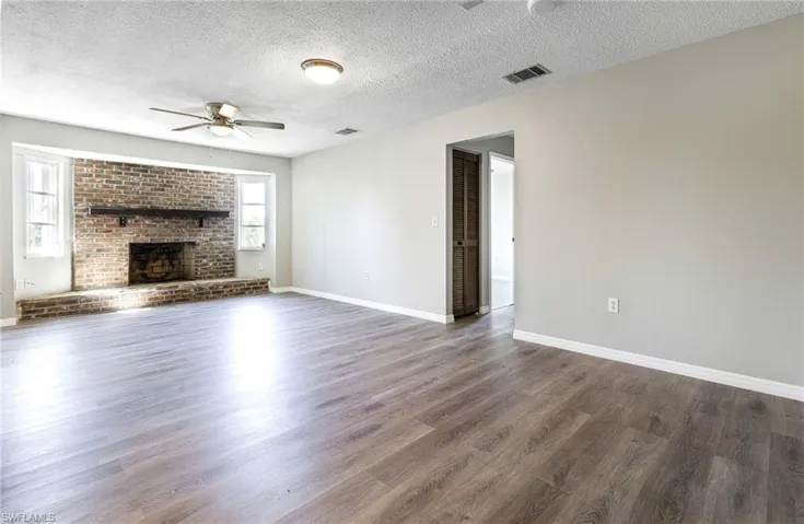 Unfurnished living room featuring a textured ceiling, dark hardwood / wood-style floors, a brick fireplace, and ceiling fan