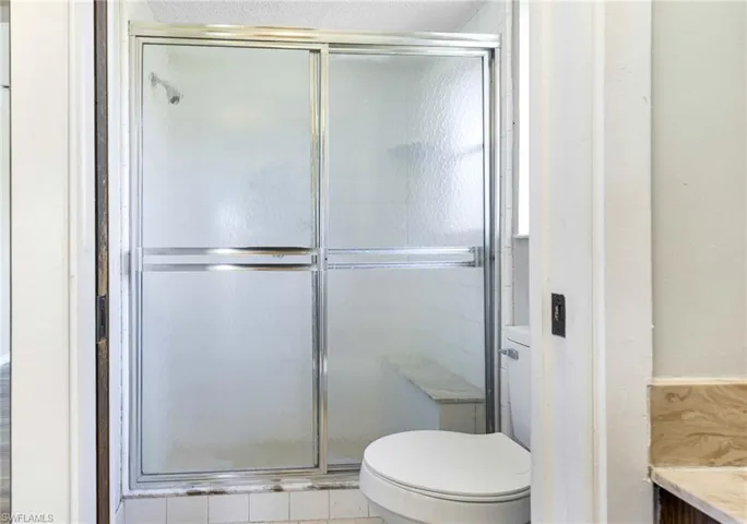 Bathroom featuring a shower with door and toilet