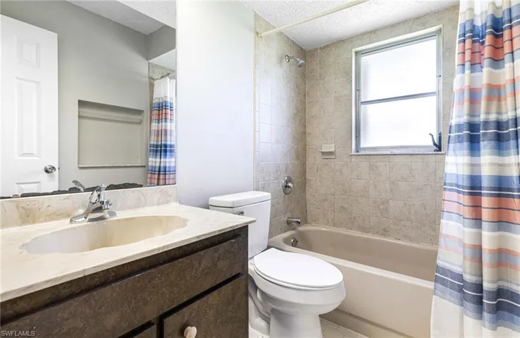 Full bathroom featuring tile flooring, a textured ceiling, shower / tub combo with curtain, toilet, and vanity