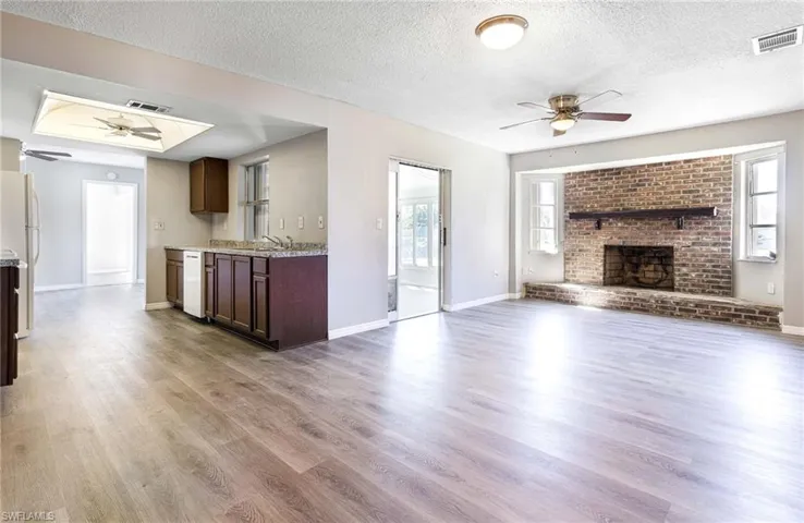 Unfurnished living room featuring ceiling fan, plenty of natural light, a fireplace, wood-type flooring, and a textured ceiling