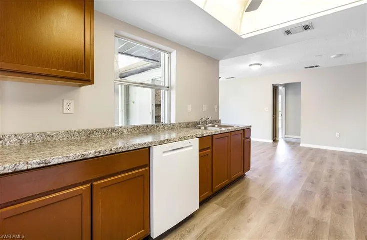 Kitchen featuring light wood-type flooring, sink, dishwasher, and light stone counters