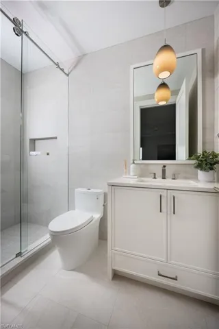 Contemporary bathroom featuring a single vanity with a white cabinet and dark hardware, set against light-toned large format tile flooring and walls