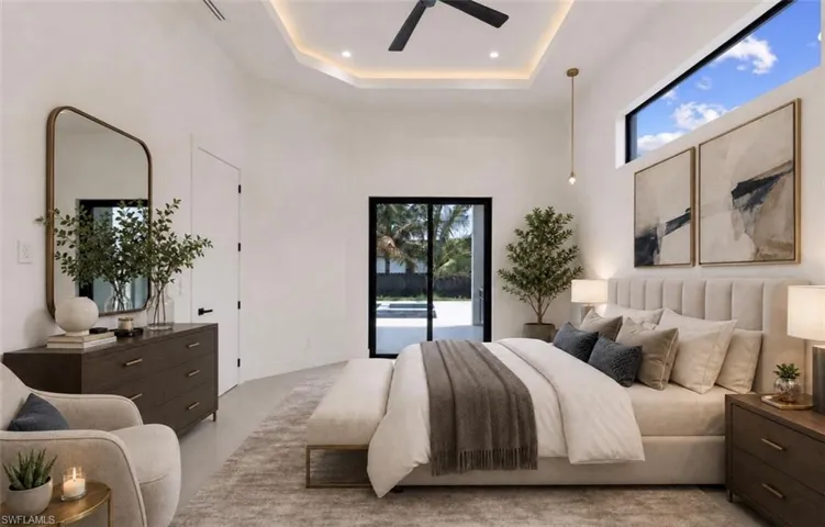 Spacious bedroom featuring a tray ceiling with recessed lighting and a ceiling fan, a large transom window, and expansive sliding glass doors providing direct access to the outdoor area