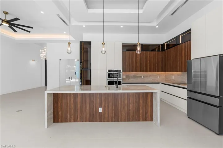 Dual tone kitchen with modern cabinets, a tray ceiling, stainless steel appliances, light stone counters, and pendant lighting