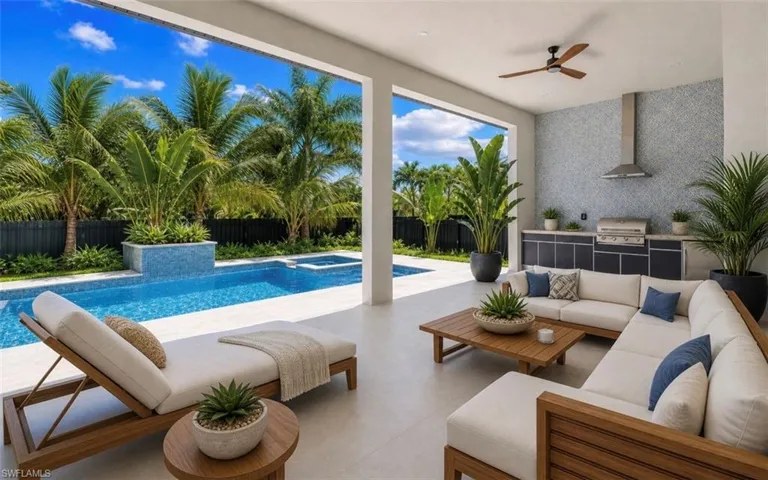 Covered outdoor living space featuring an integrated kitchen with a stainless steel grill and range hood, mosaic tile backsplash, and a ceiling fan