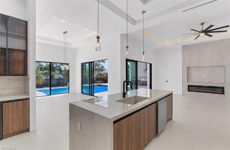 Kitchen featuring modern cabinets, open floor plan, a tray ceiling, light stone countertops, and glass insert cabinets