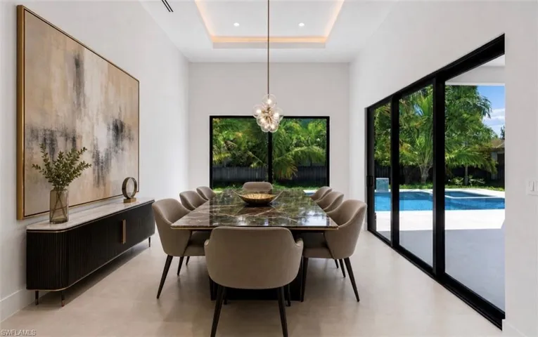 Dining area featuring a recessed ceiling with integrated lighting, a contemporary chandelier, large format tile flooring, and a full wall of sliding glass doors opening to a pool patio