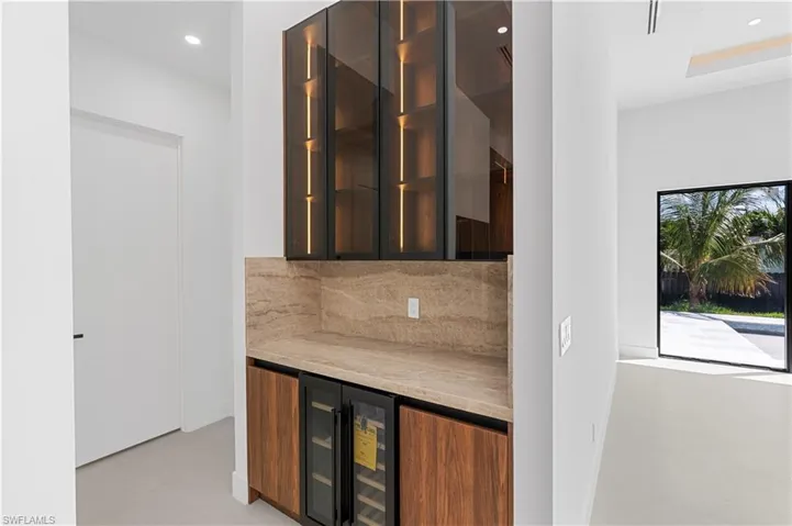 Bar area featuring modern cabinets, recessed lighting, wine cooler, light stone countertops, and glass insert cabinets