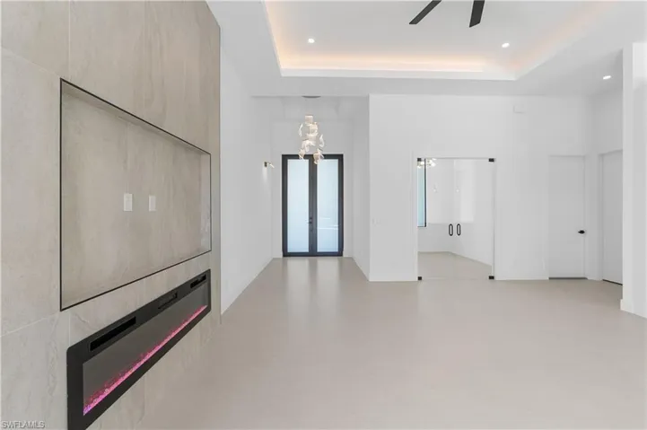 Unfurnished living room featuring french doors, a ceiling fan, a raised ceiling, a large fireplace, and recessed lighting