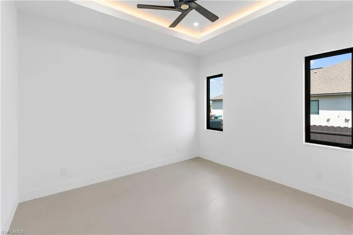 Unfurnished room featuring a raised ceiling, finished concrete floors, and a ceiling fan