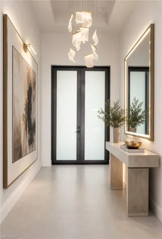 Modern entryway featuring a sculptural chandelier, large format light-toned tile flooring, and double entry doors with frosted glass