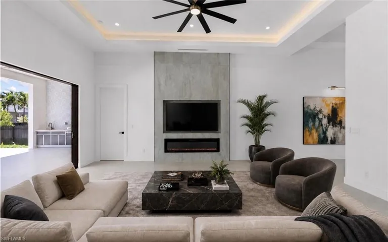 Spacious living area featuring a modern fireplace with a textured surround, recessed lighting, a ceiling fan, and large sliding doors opening to an outdoor area with built-in cabinetry