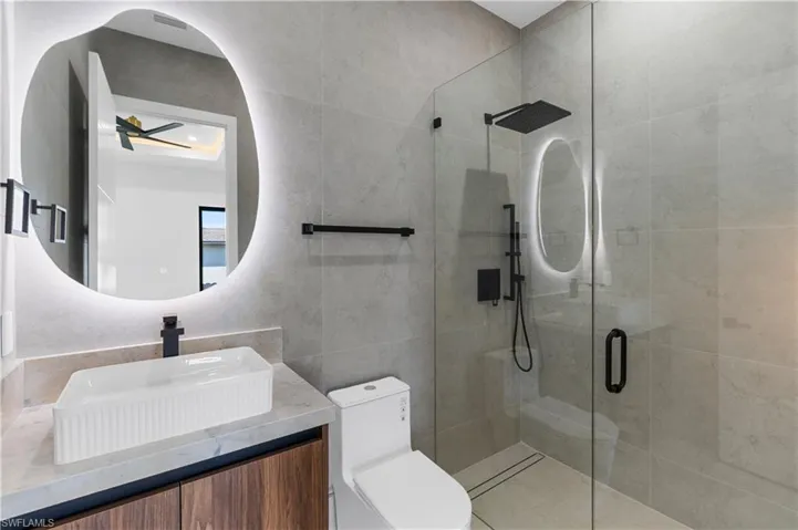 Full bath with a shower stall, vanity, tile walls, and a ceiling fan