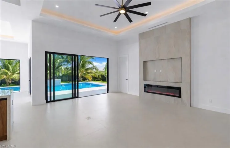 Unfurnished living room with ceiling fan, a high tray ceiling, a fireplace, and recessed lighting