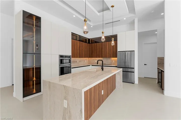 Kitchen with modern cabinets, stainless steel appliances, dual tone cabinets, light stone countertops, and decorative light fixtures