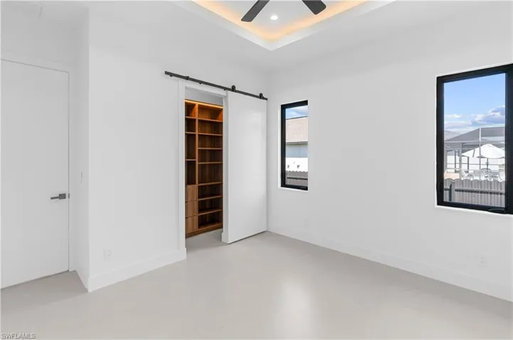Empty room featuring a barn door, concrete flooring, a tray ceiling, ceiling fan, and recessed lighting