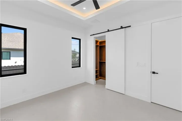 Unfurnished bedroom featuring a barn door, concrete flooring, a walk in closet, a raised ceiling, and ceiling fan