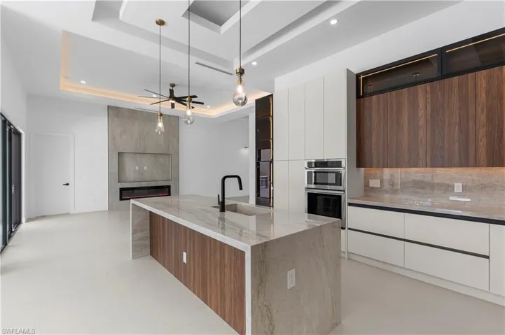 Two tone kitchen featuring modern cabinets, two tone color scheme, light stone counters, open floor plan, and a tray ceiling