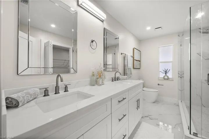 Full bathroom featuring double vanity, a marble finish shower, light marble finish floors, and recessed lighting
