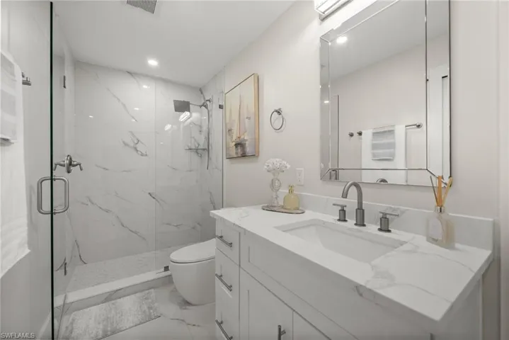 Full bathroom with vanity, a marble finish shower, light marble finish flooring, and recessed lighting