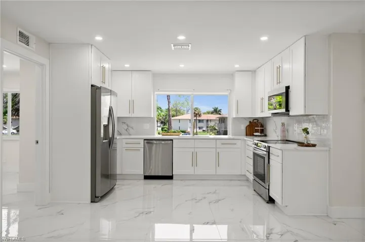 Kitchen featuring light marble finish flooring, tasteful backsplash, white cabinetry, appliances with stainless steel finishes, and recessed lighting