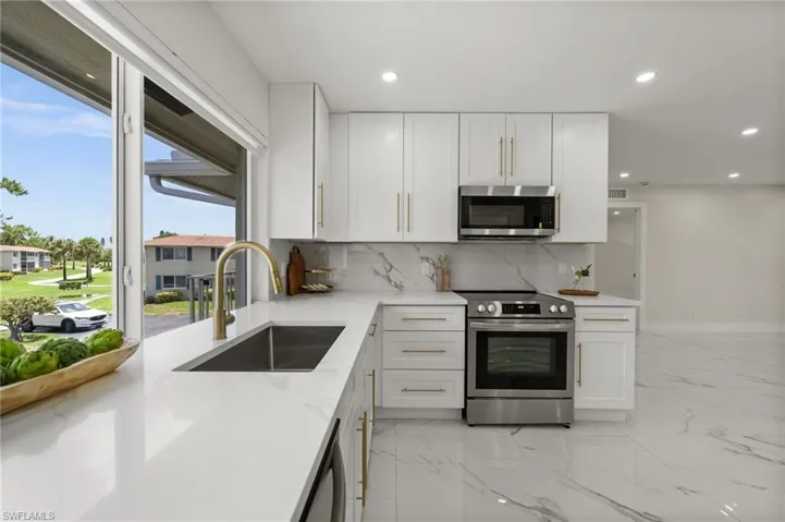 Kitchen featuring stainless steel appliances, white cabinets, light marble finish floors, decorative backsplash, and recessed lighting