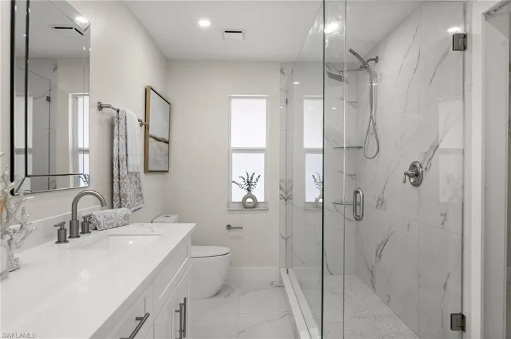Bathroom featuring vanity, a marble finish shower, light marble finish flooring, and recessed lighting