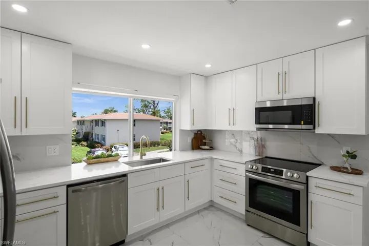 Kitchen featuring appliances with stainless steel finishes, decorative backsplash, light marble finish flooring, white cabinetry, and recessed lighting