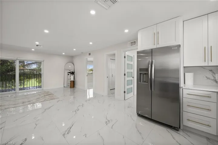 Kitchen with stainless steel fridge with ice dispenser, recessed lighting, light marble finish floors, white cabinetry, and open floor plan