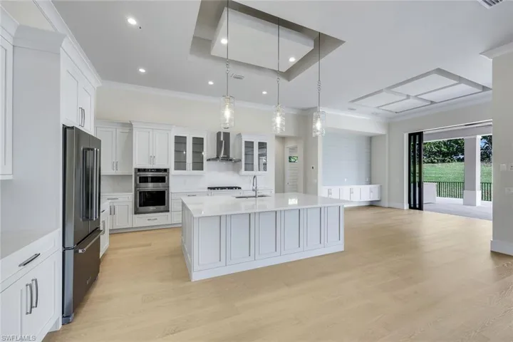Kitchen with tasteful backsplash, glass insert cabinets, hanging light fixtures, white cabinets, and light stone countertops