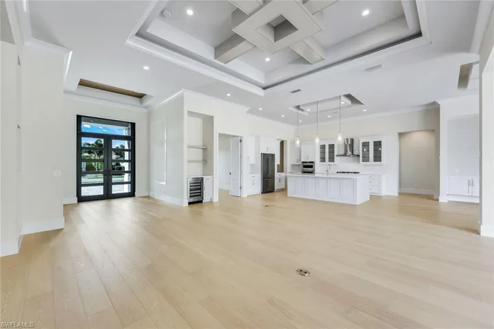 Unfurnished living room with light wood-style flooring, recessed lighting, coffered ceiling, wine cooler, and ornamental molding