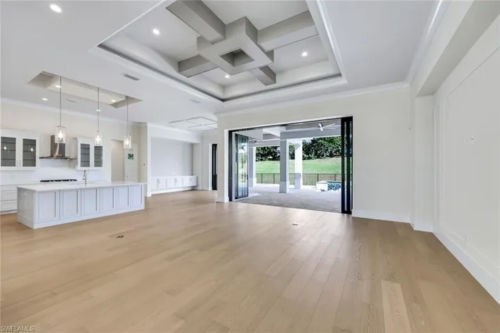 Unfurnished living room with coffered ceiling, light wood-style floors, crown molding, beamed ceiling, and a tray ceiling