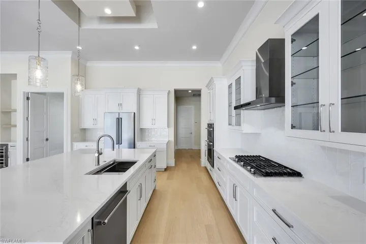 Kitchen with backsplash, ornamental molding, light stone counters, pendant lighting, and white cabinetry